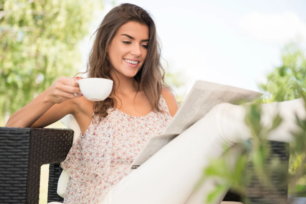 Pessoa tomando café da manhã com jornal perto da janela
