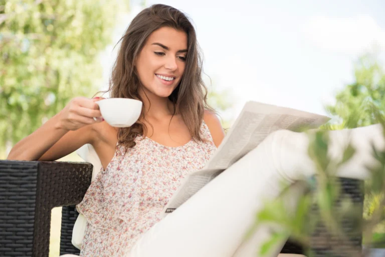 Pessoa tomando café da manhã com jornal perto da janela